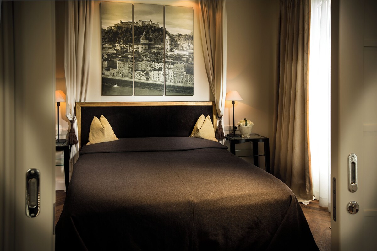 A hotel room with a large bed, two bedside tables, and a cityscape view through the window.