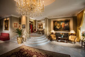 Un lobby imponente con una escalera de mármol, un candelabro y un cuadro clásico de grandes dimensiones.