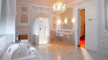 A spacious bathroom with a large bathtub, two sinks, a shower, and a chandelier.