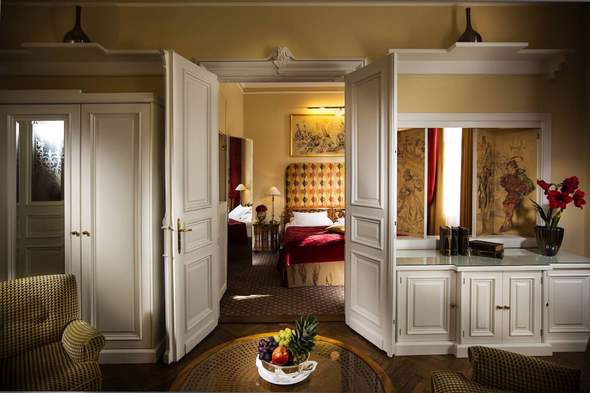 Ein Hotelzimmer mit Bett, Sitzecke mit Stühlen, Esstisch mit Obst und einem großen Spiegel.