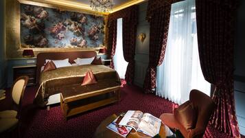 A luxurious bedroom with a large bed, a chandelier, a red carpet, and a large window with curtains.