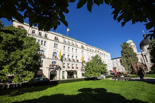 Un edificio grande e histórico con una entrada central, rodeado de céspedes y árboles bien cuidados.