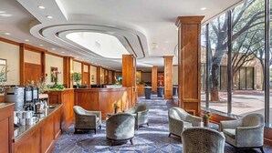 A hotel lobby with a reception desk, seating area, and large windows offering a view of the outdoors. - Austin Southpark Hotel (Austin)