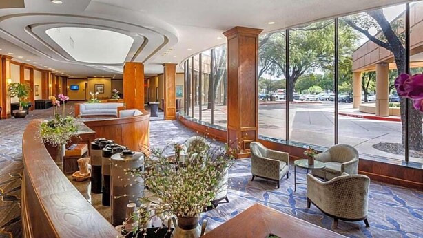 A hotel lobby with a reception desk, seating area, and large windows offering a view of the street. - Austin Southpark Hotel (Austin)