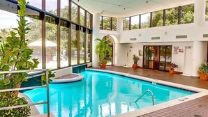 An indoor swimming pool with clear glass walls, surrounded by potted plants and a tiled floor. - Austin Southpark Hotel (Austin)