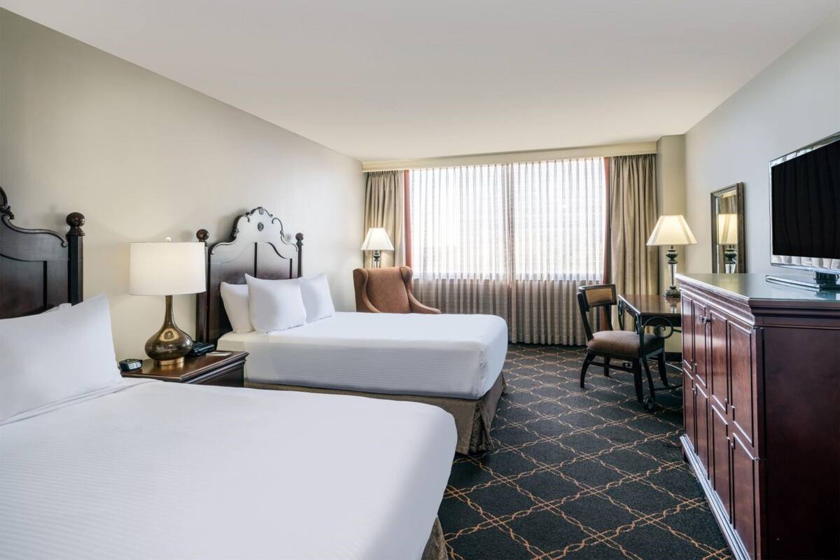 A hotel room with two beds, a television, a desk, and a chair.
