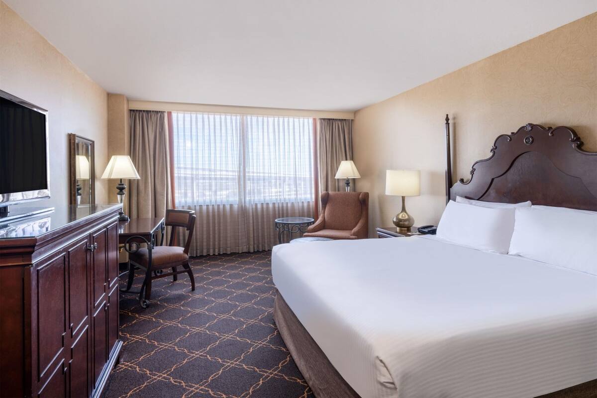 A hotel room with a large bed, a desk with a chair, a television, and two lamps.