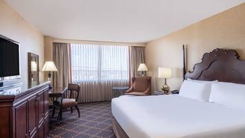 A hotel room with a large bed, a desk with a chair, a television, and two lamps.