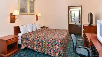 Habitación de hotel con cama, escritorio, silla, televisión y dos lámparas de pared.