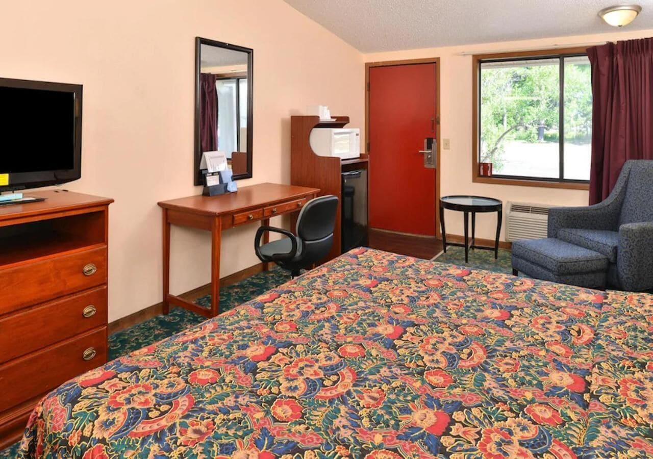 Habitación de hotel con una cama grande, un escritorio con silla, televisor, microondas y ventana con cortinas.