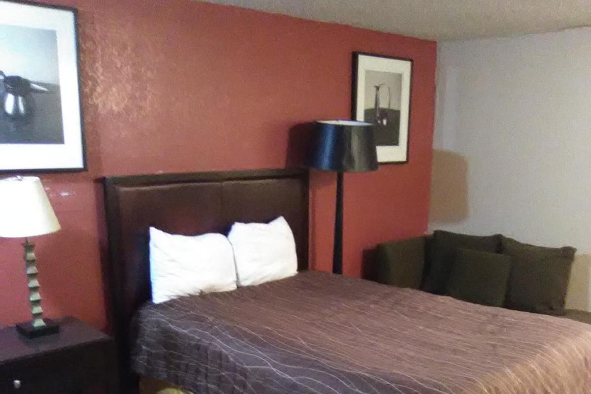A hotel room with a bed, a nightstand, a lamp, and a framed picture on the wall.