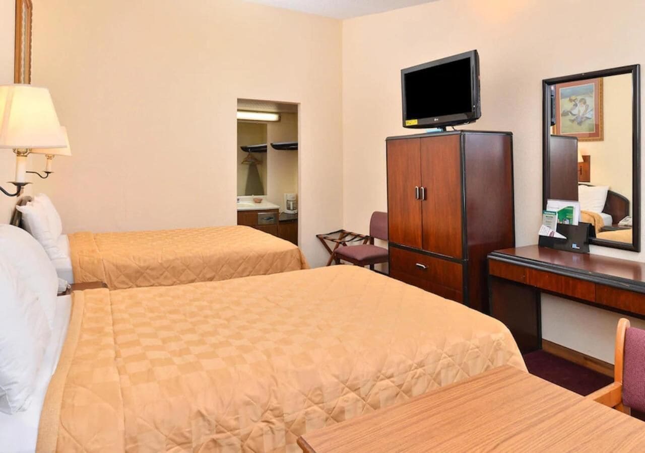 A hotel room with two beds, a desk, a television, and a mirror.