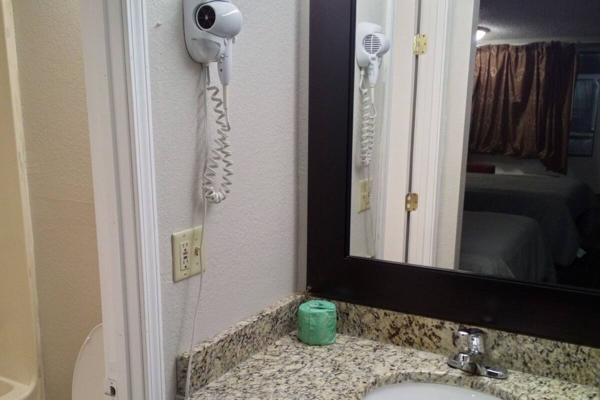 A bathroom with a white toilet, a granite countertop sink, a green soap dispenser, and a hairdryer mounted on the wall.