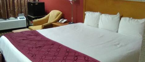 A hotel room with a large bed, a desk with a lamp, a chair, and a television.