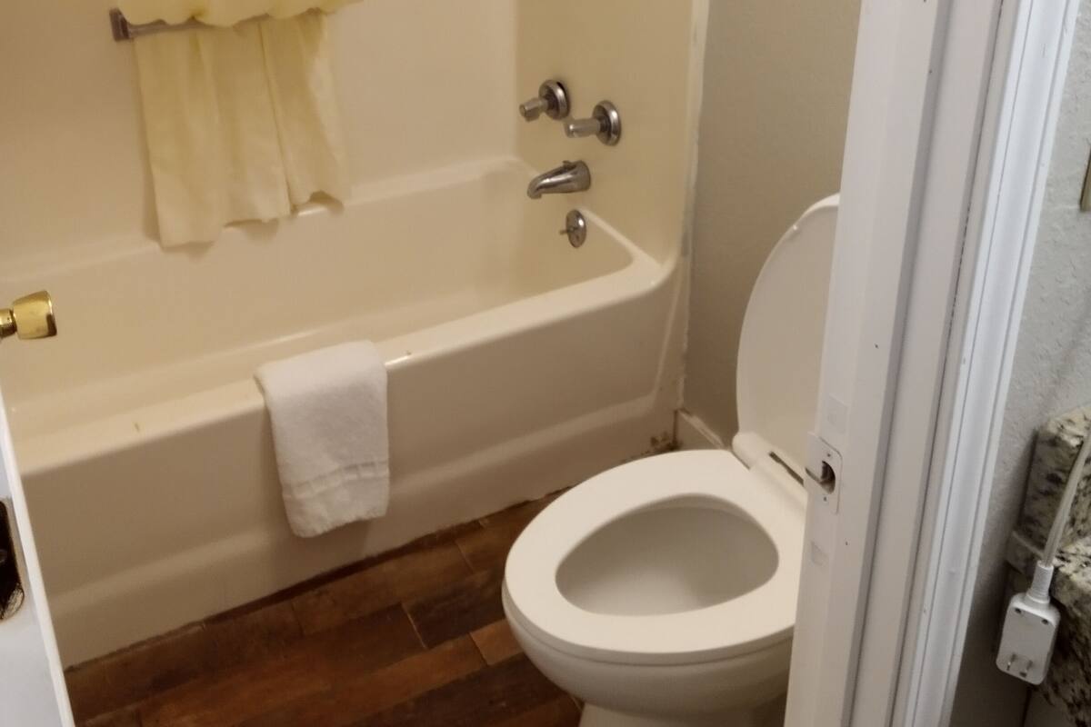 A bathroom with a bathtub, toilet, and wooden flooring.