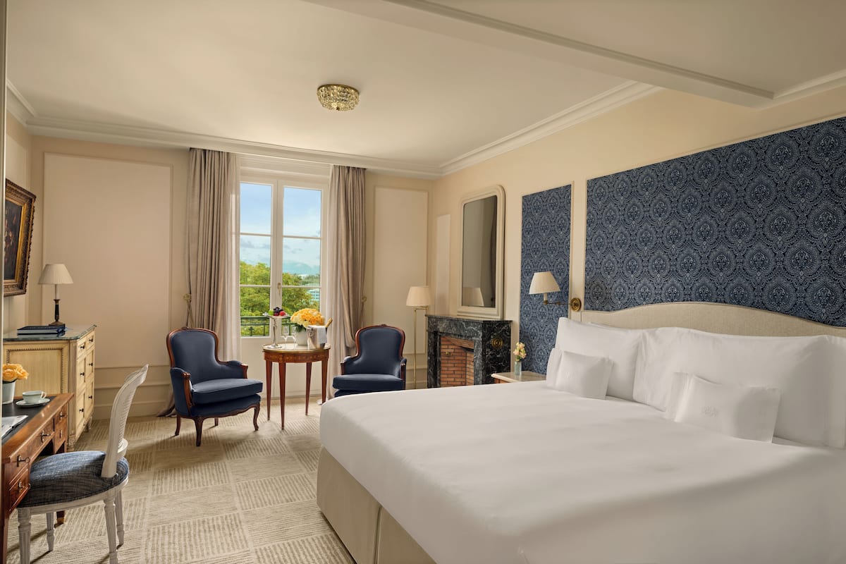 A hotel room with a large bed, two armchairs, a desk, and a fireplace.
