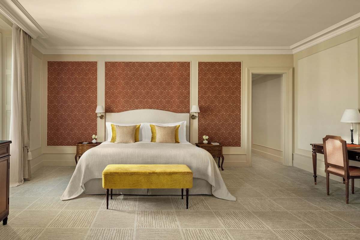 A hotel room with a large bed, a desk, a chair, and a television.