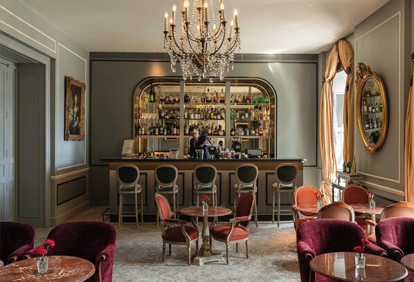 A bar area with a bartender, multiple bar stools, and a well-stocked liquor shelf. There are several round tables with chairs in the foreground.