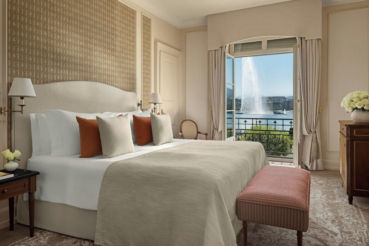 A hotel room with a large bed, a view of a fountain, and a balcony with curtains.