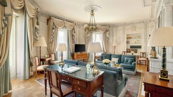 A spacious living room with a glass coffee table, a blue sofa, and a wooden desk with a lamp.