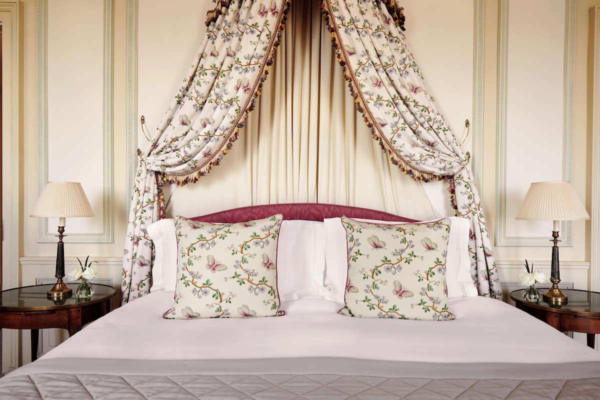 A large bed with floral-patterned pillows, a canopy, and two bedside tables with lamps.