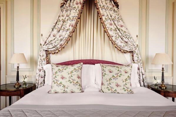 A large bed with floral-patterned pillows, a canopy, and two bedside tables with lamps.