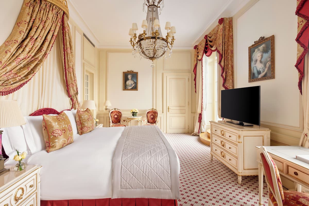 A bedroom with a large bed, a television, a dresser, and a desk.
