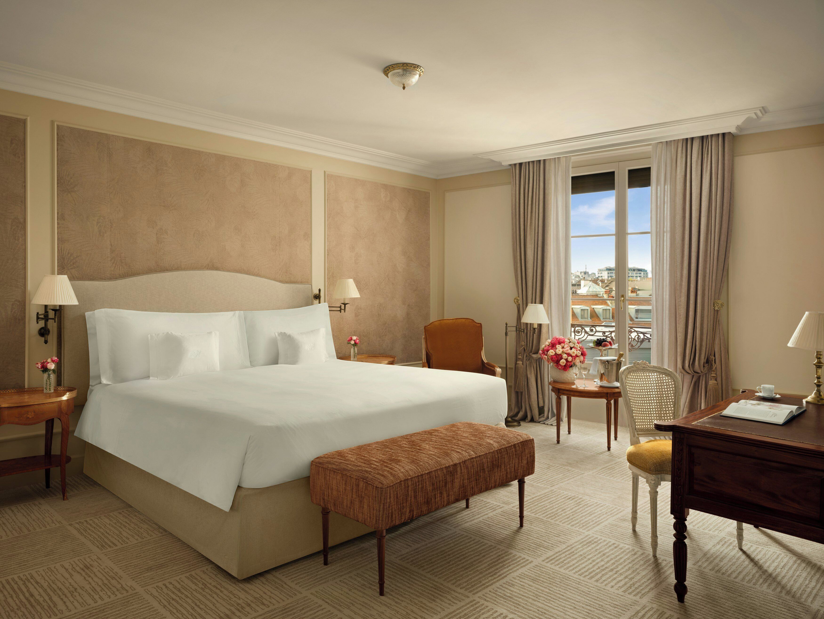 A hotel room with a large bed, a wooden bench, a desk, and a chair.