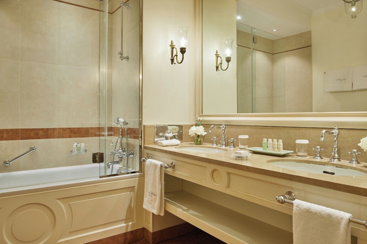 Un baño moderno con ducha envuelta en vidrio, un tocador amplio con lavamanos dobles y un espejo grande sobre el lavamanos.