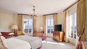 A hotel room with a large bed, a desk, a television, and a view of the city. - Beau Rivage Geneva (Geneva)