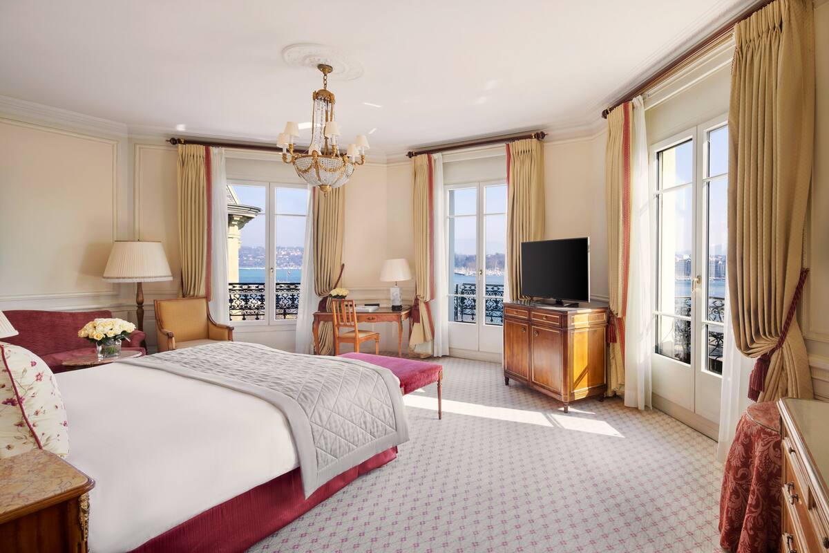 A hotel room with a large bed, a desk, a television, and a view of the city.