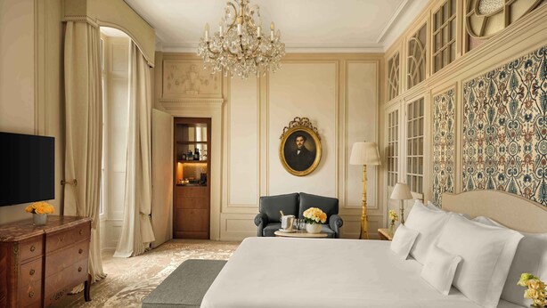 A luxurious bedroom with a large bed, a television, a desk with drawers, a chair, and a chandelier. - Beau Rivage Geneva (Geneva)
