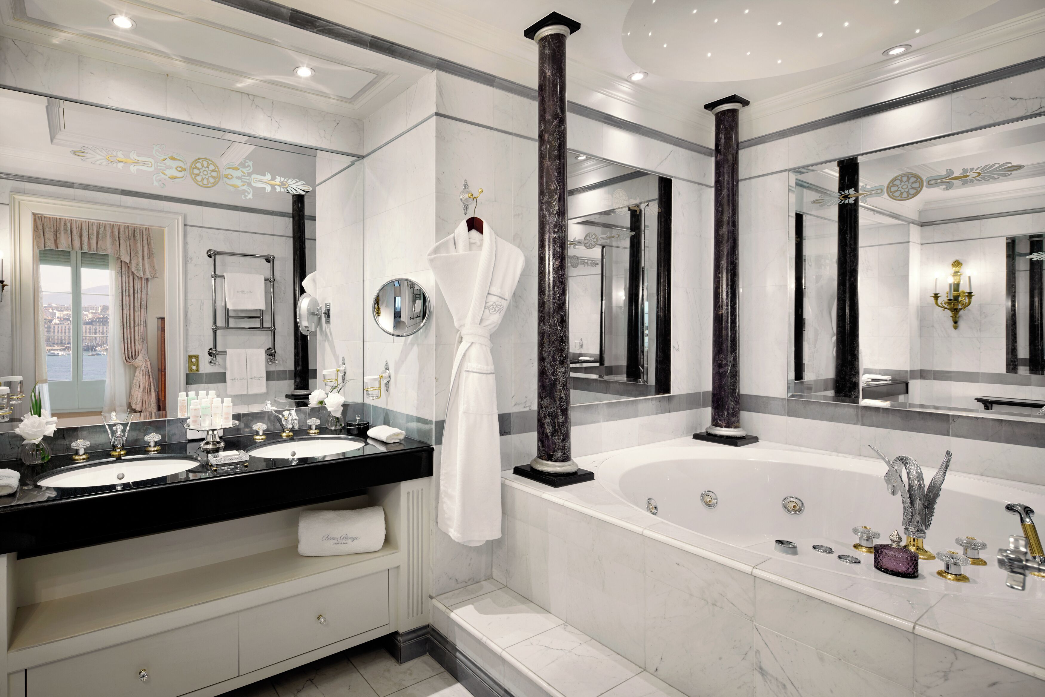 A luxurious bathroom with two sinks, a large bathtub, and a mirror with a decorative frame.