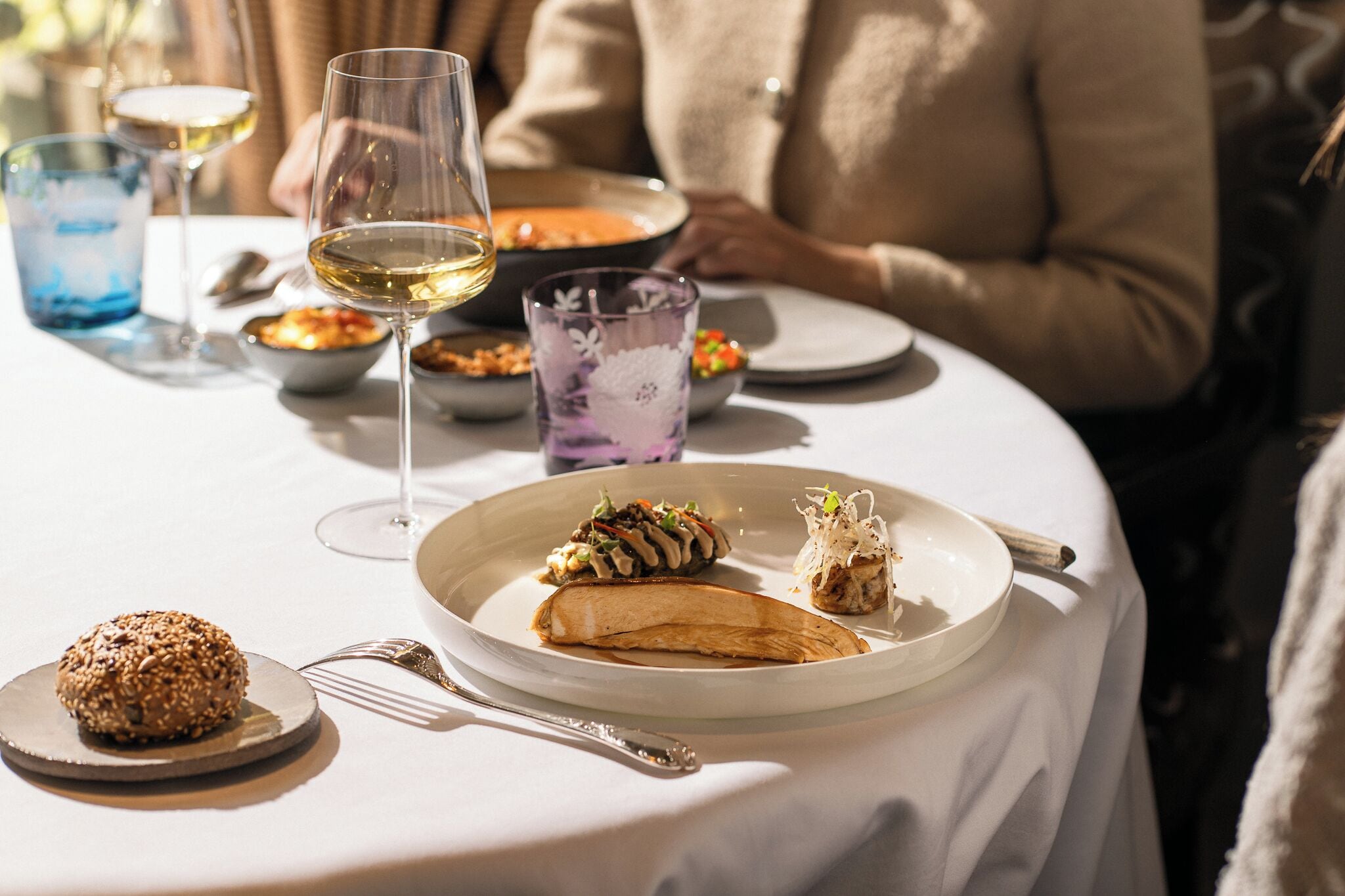 A dining table with plates of food, a wine glass, and a bowl of soup.
