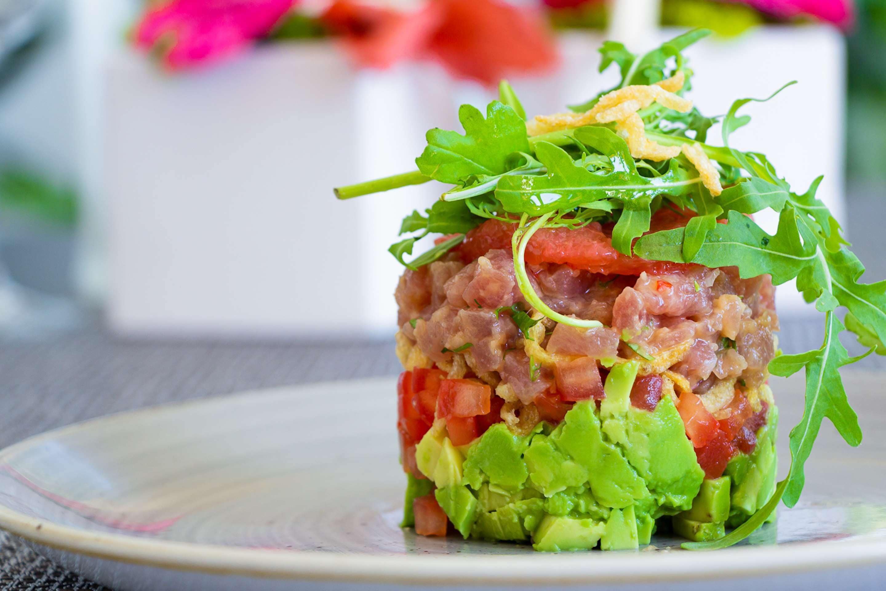 Insalata a strati con verdure a foglia, pomodori e avocado su un piatto.