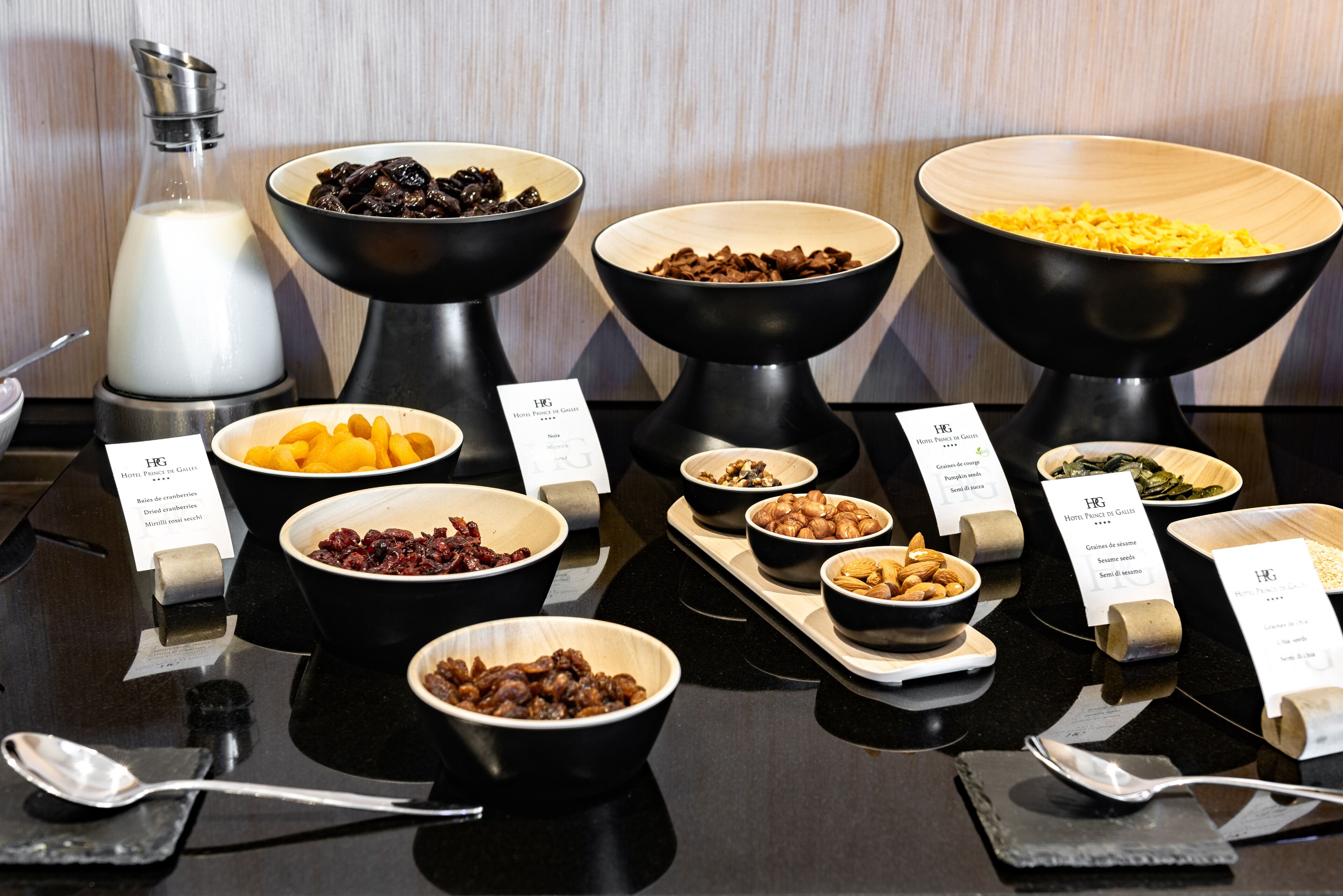 Un buffet proposant divers plats présentés dans des bols noirs et en bois, accompagnés de petites étiquettes.
