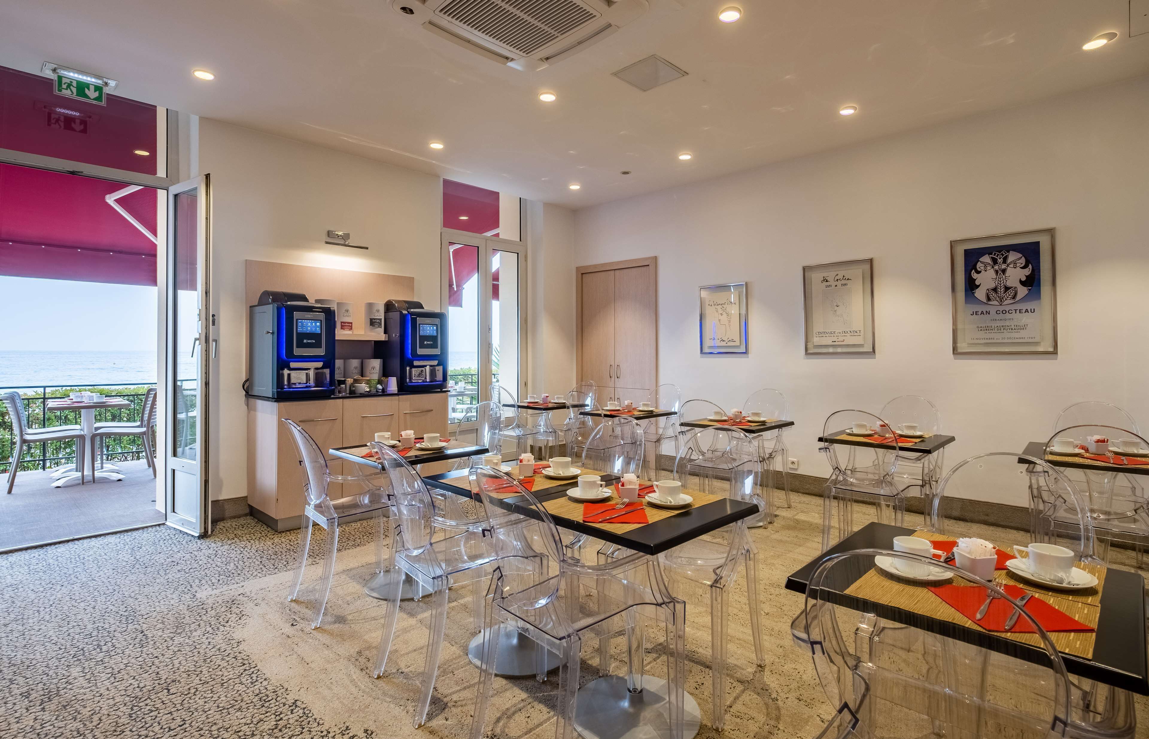A modern dining area with clear chairs and tables, equipped with digital coffee machines, and framed certificates on the wall.