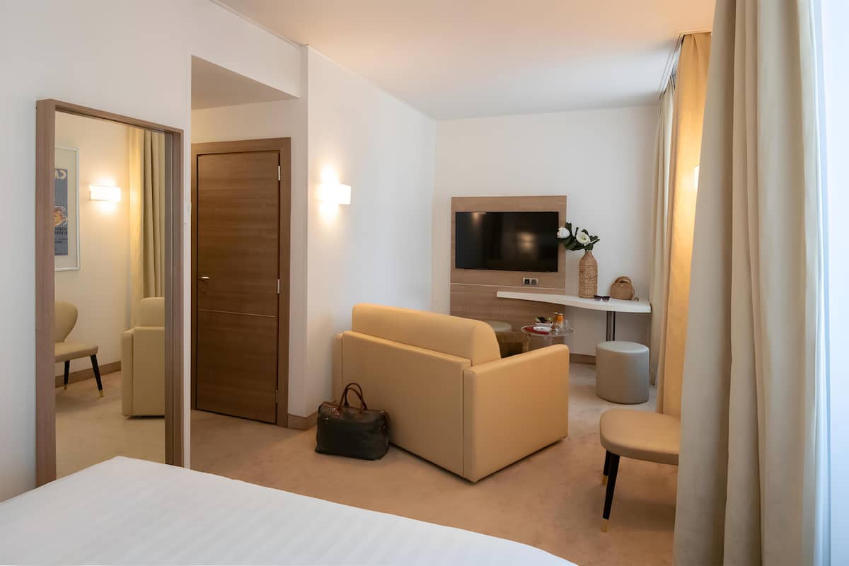 A hotel room with a bed, a sofa, a TV, a small table, and a chair.