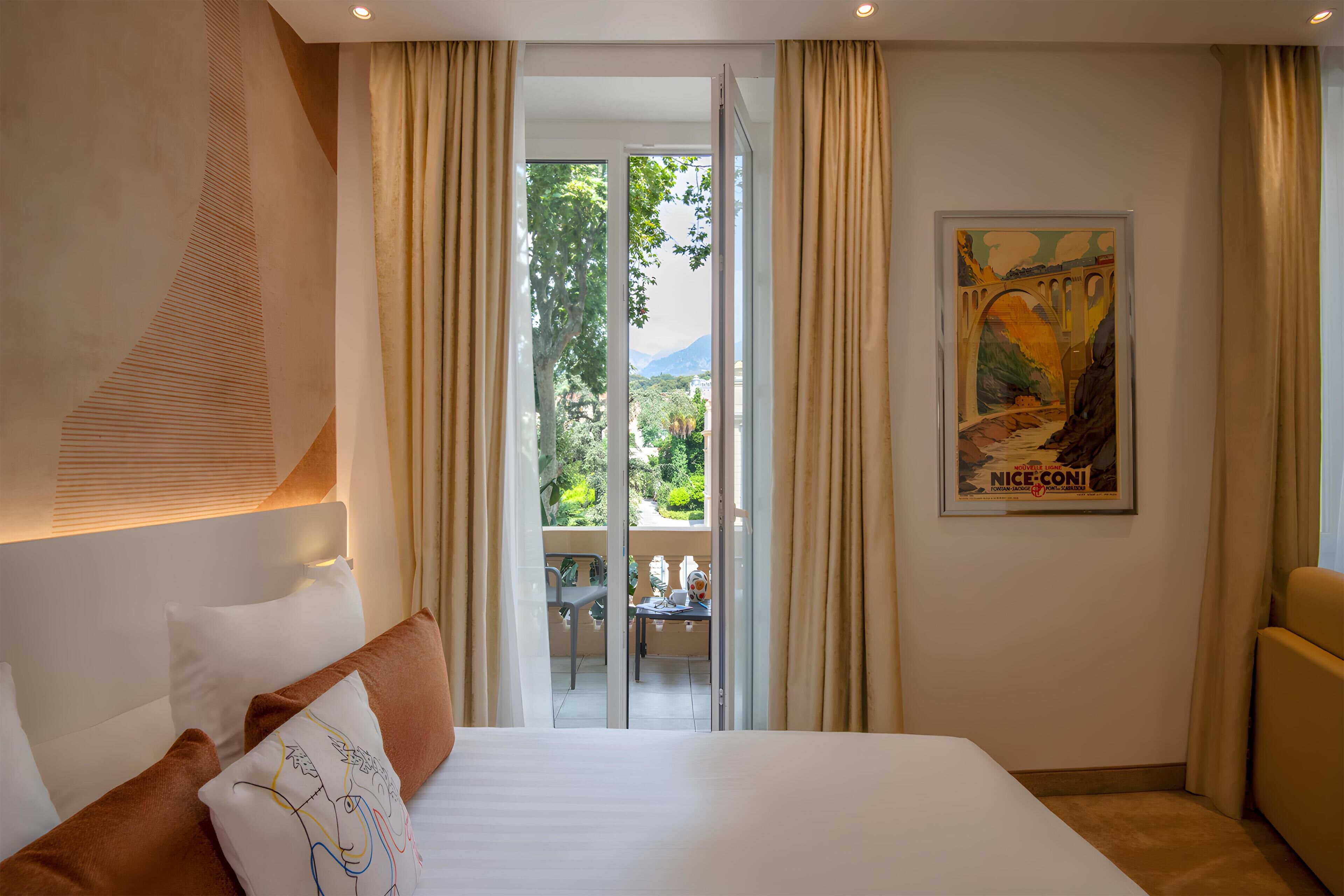 A hotel room with a bed, a view of a balcony, and a poster on the wall.