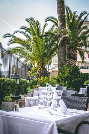 Un espacio de comedor al aire libre con mesas dispuestas para una comida, rodeado de palmeras y vegetación.