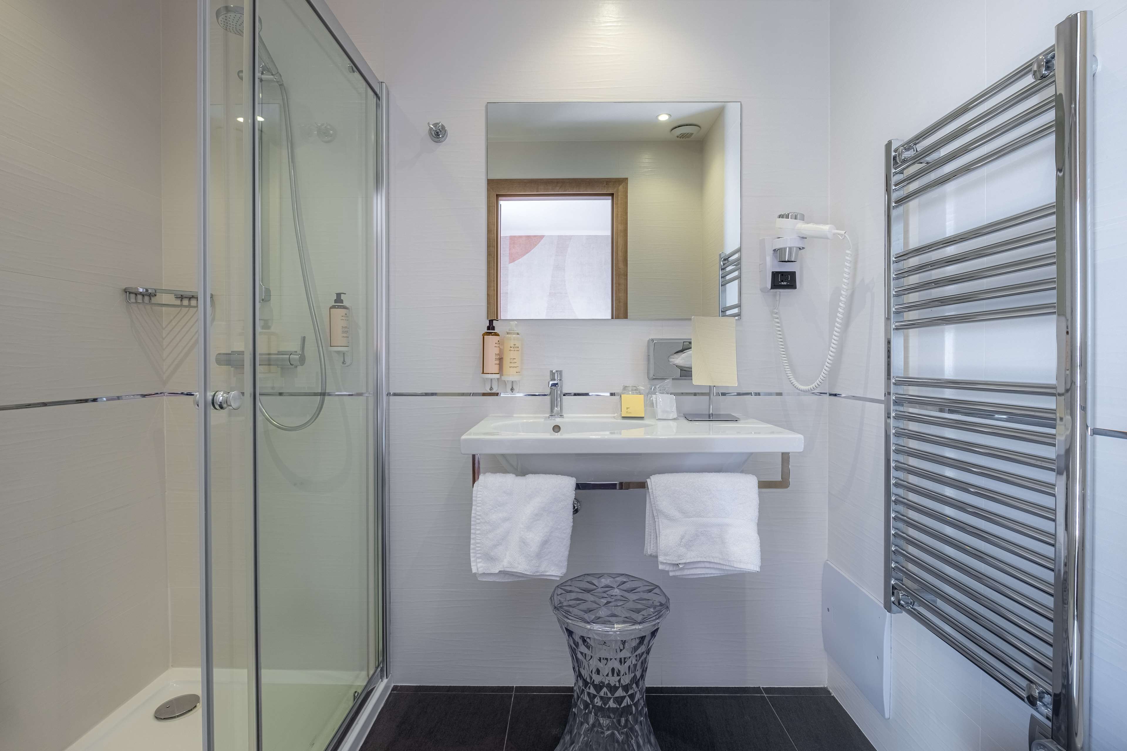 Un baño moderno con ducha de vidrio, lavamanos blanco y un espejo encima, además de un perchero para toallas.