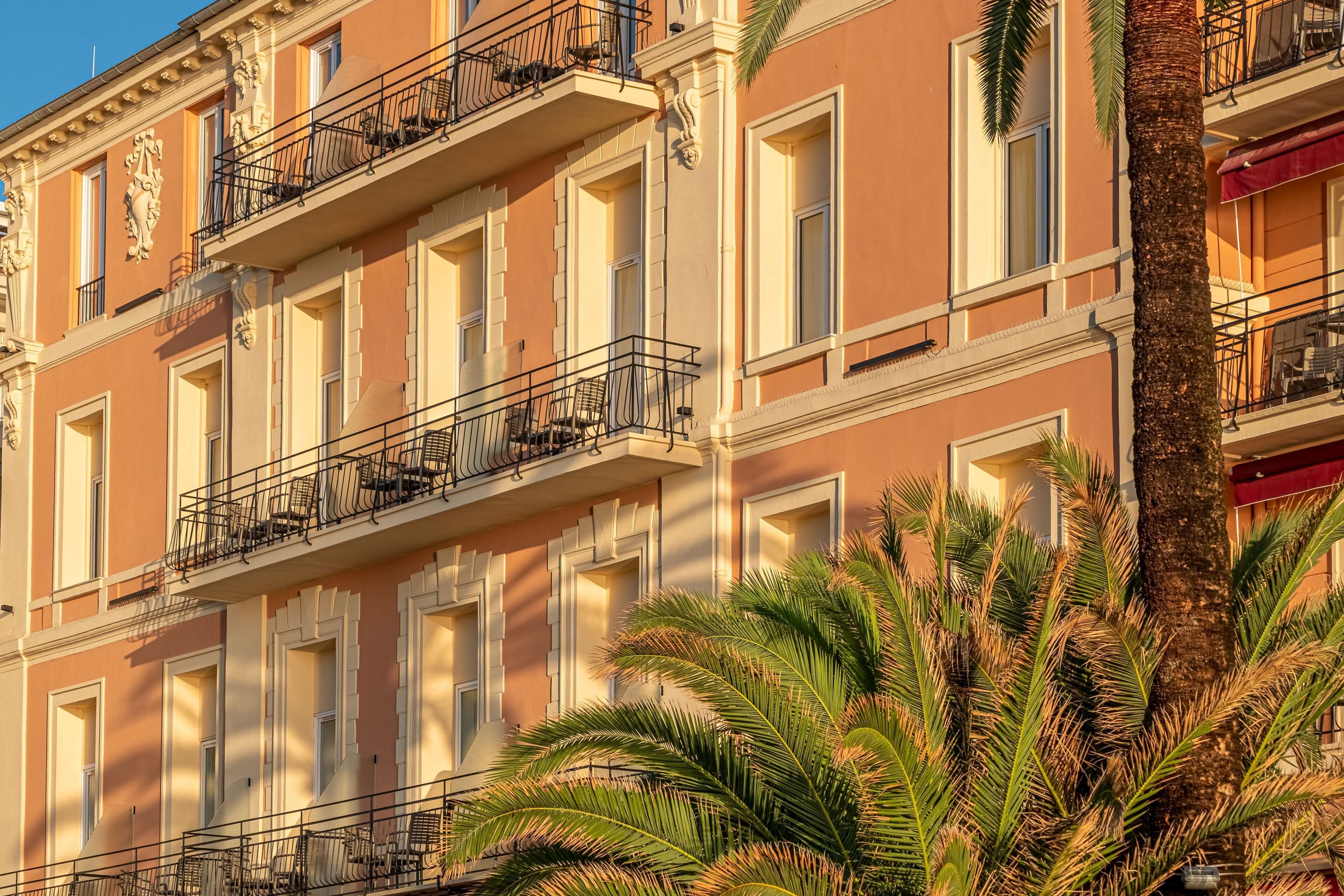 Un immeuble à plusieurs étages doté de balcons, de grandes fenêtres et d’un palmier au premier plan.