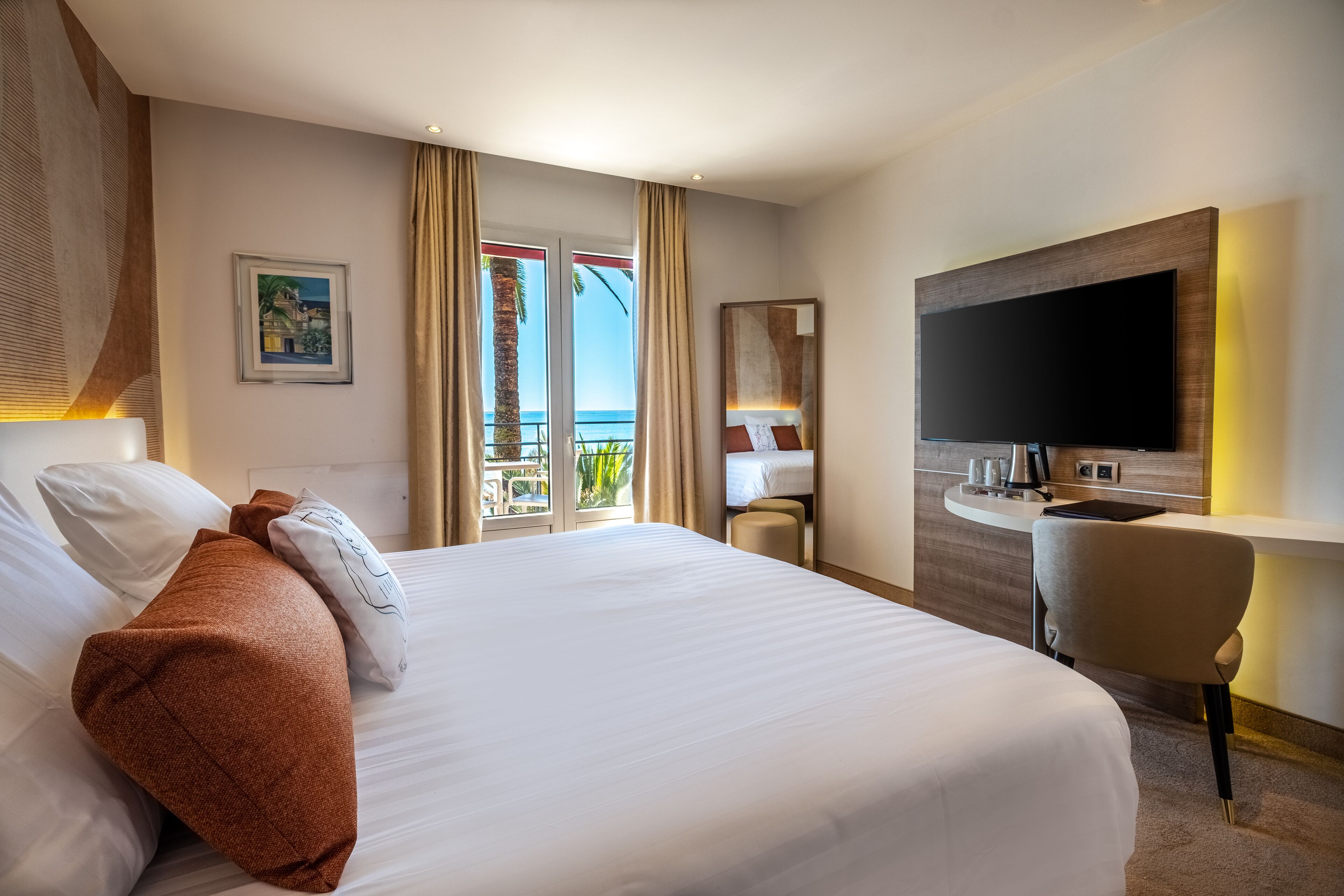 A hotel room with a large bed, a desk, a flat-screen TV, and a balcony with a view.