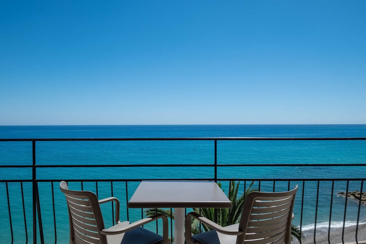 A balcony with two chairs and a table overlooking a clear blue sea.