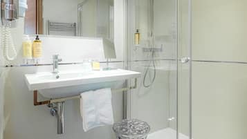Une salle de bain moderne avec une douche à parois de verre, un lavabo blanc avec un miroir au-dessus et une poubelle en verre.