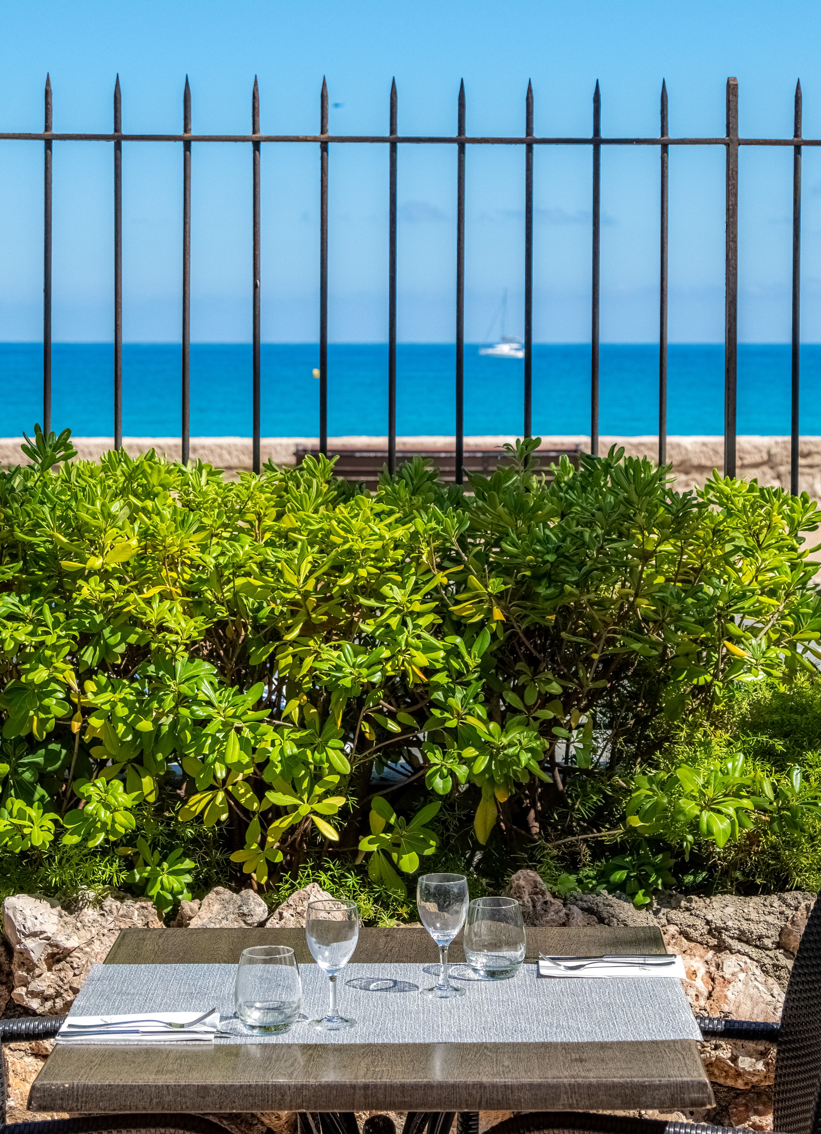 A table with empty glasses and a view of the ocean through a metal fence.