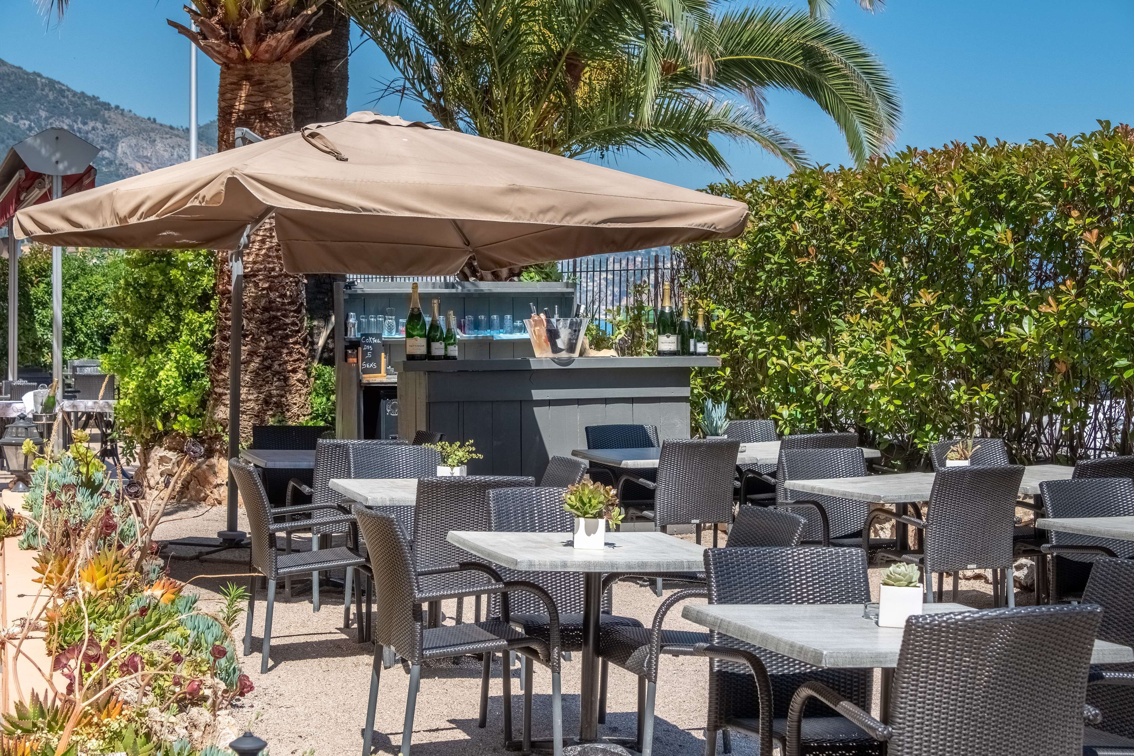 Un espacio al aire libre con mesas y sillas, una zona de bar con botellas y una palmera.