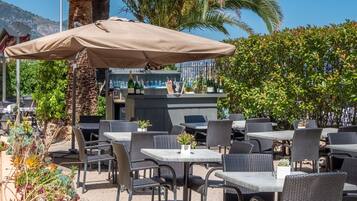Un espacio al aire libre con mesas y sillas, una zona de bar con botellas y una palmera.