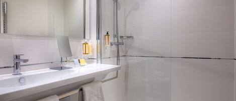 A modern bathroom with a glass-enclosed shower, a white sink with a mirror, and a towel rack.