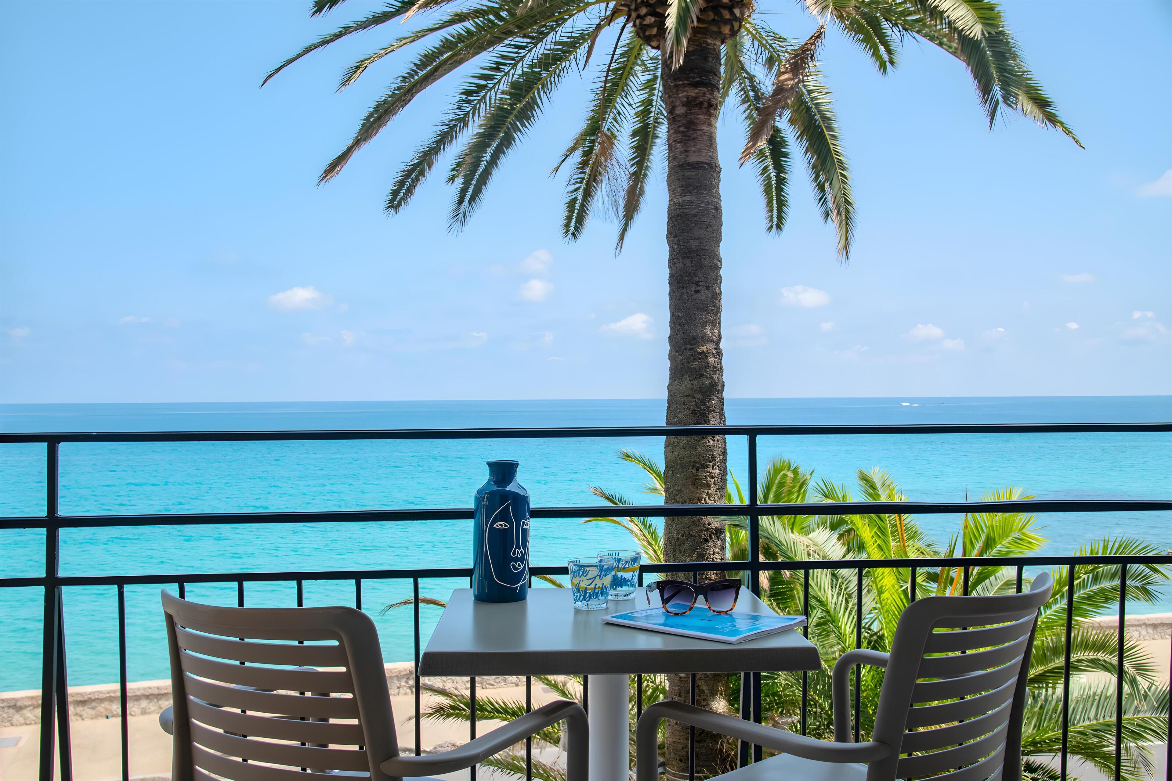 A balcony with a table, chairs, a vase, and a pair of sunglasses.